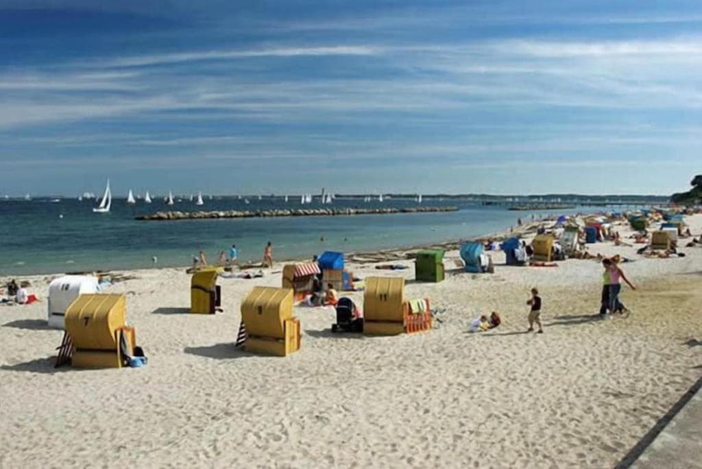 Ostseestrand mit bunten Strandkörben, Badegästen und Segelbooten auf der Kieler Förde