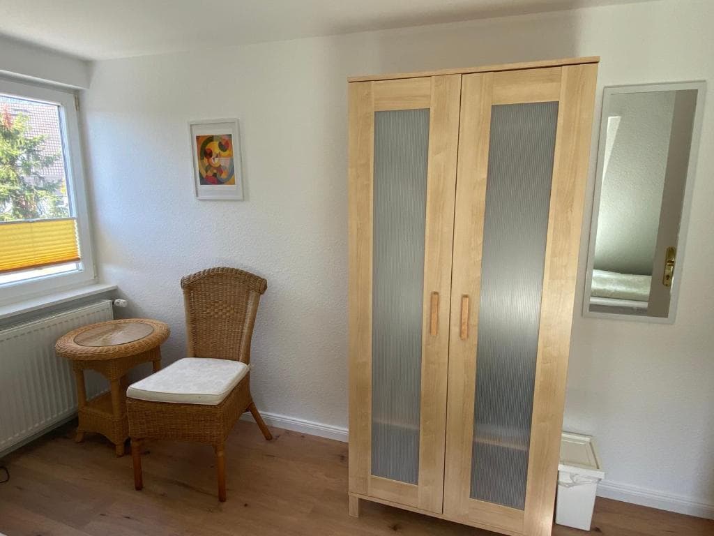 Schlafzimmer mit hellem Kleiderschrank mit Glastüren und Korbstuhl