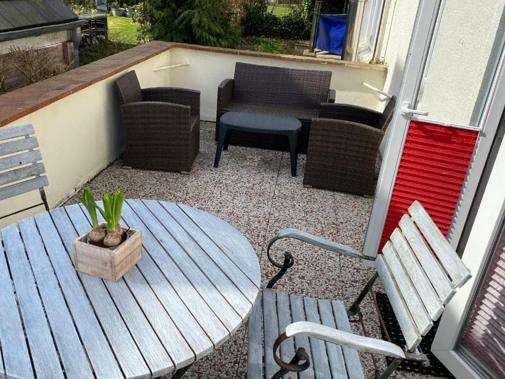 Kiesterrasse mit rundem Holztisch, Bänken und Rattan-Loungemöbeln