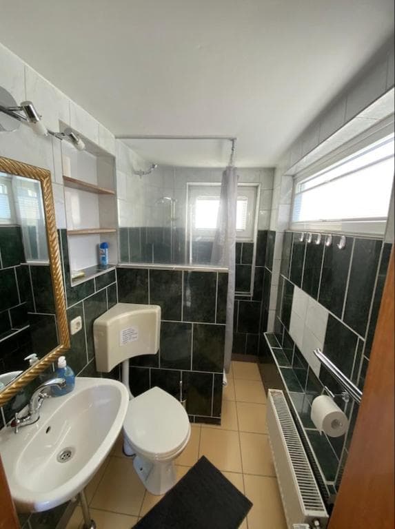 Duschbad mit grünen Fliesen, Waschbecken und goldgerahmtem Spiegel