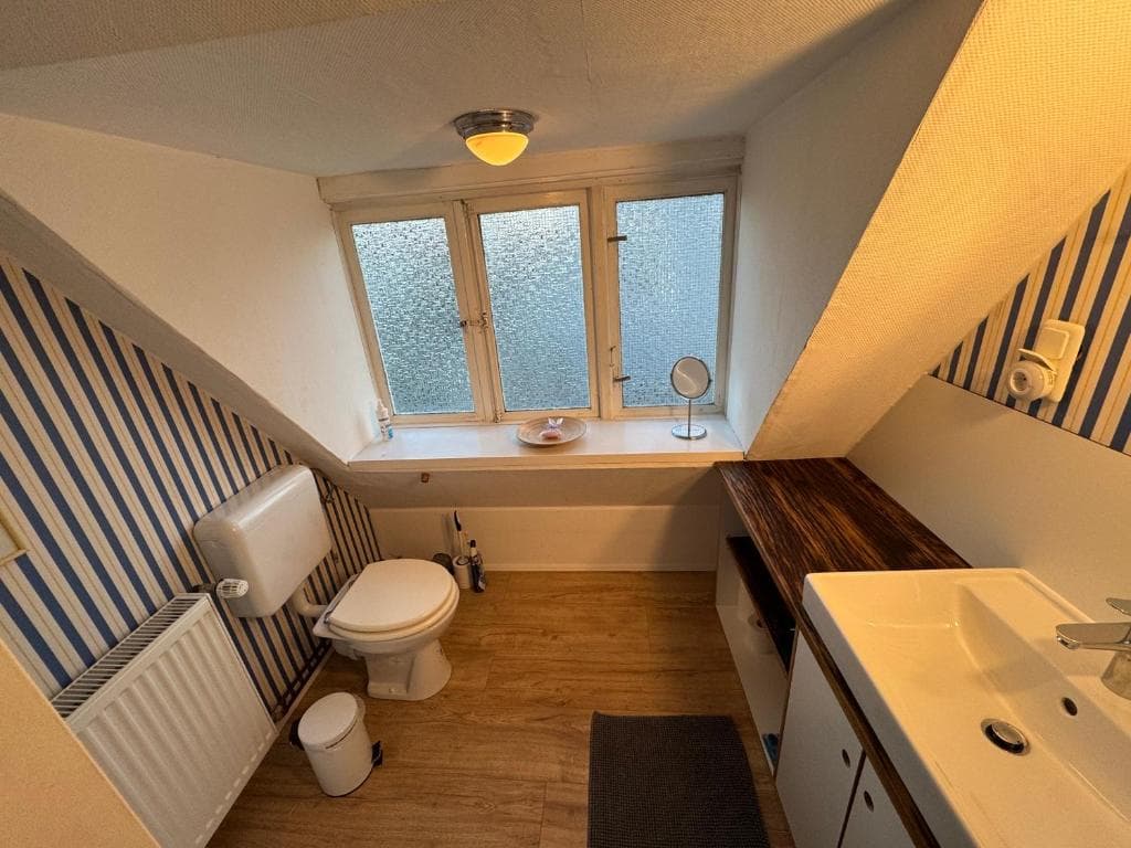 Gäste-WC mit blau gestreifter Tapete, Badewanne und Holzablage
