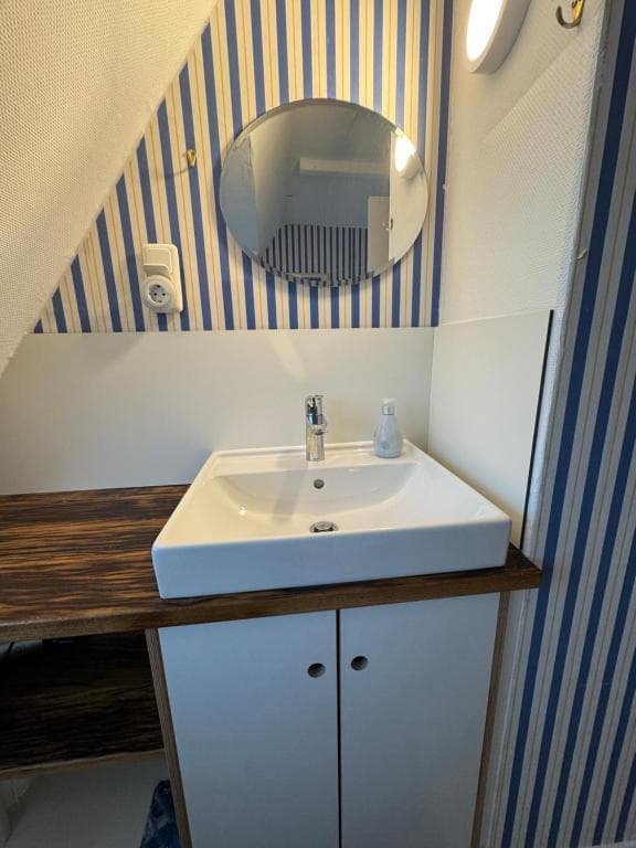 Waschbecken mit rundem Spiegel vor blau gestreifter Tapete